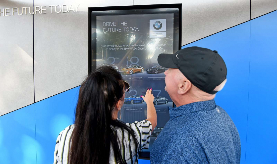 woman and man interacting with BMW interactive touchscreen app displayed on grey and blue wall