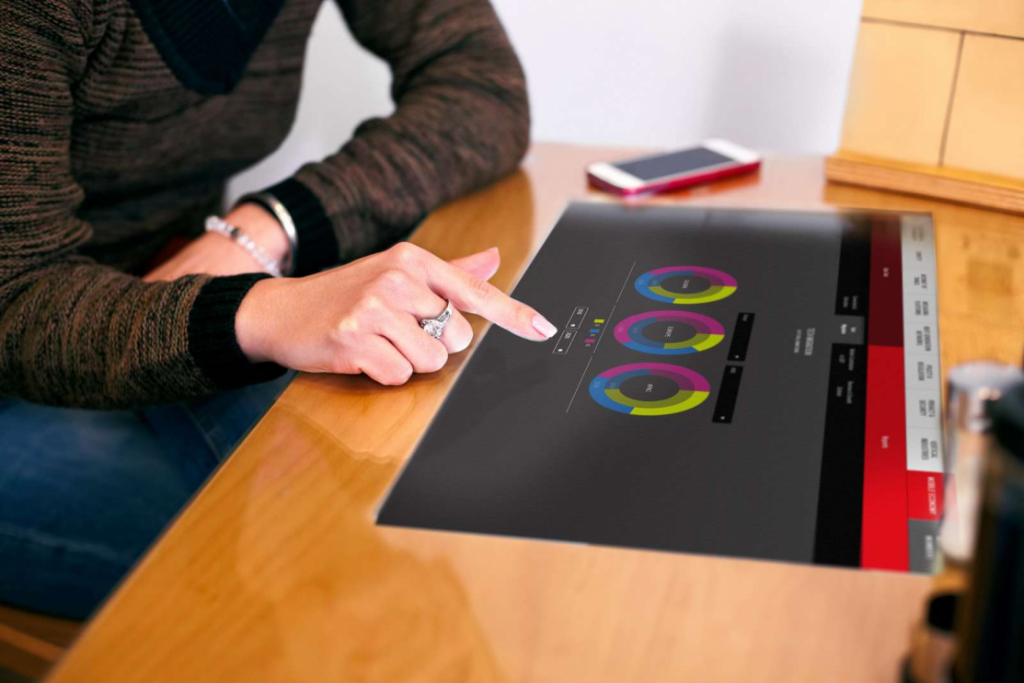 person wearing diamond ring interacting with interactive touchscreen presentation displayed on large monitor on wooden table