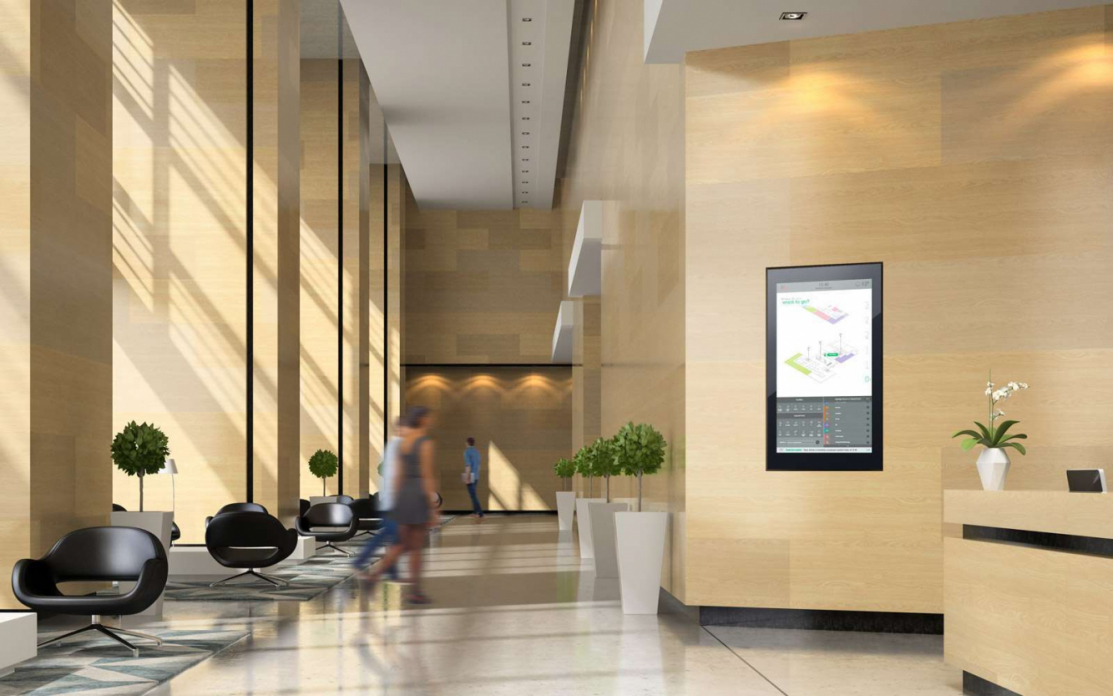 People walking through light beige wooden walled office reception with interactive touchscreen displayed between plants on right hand side