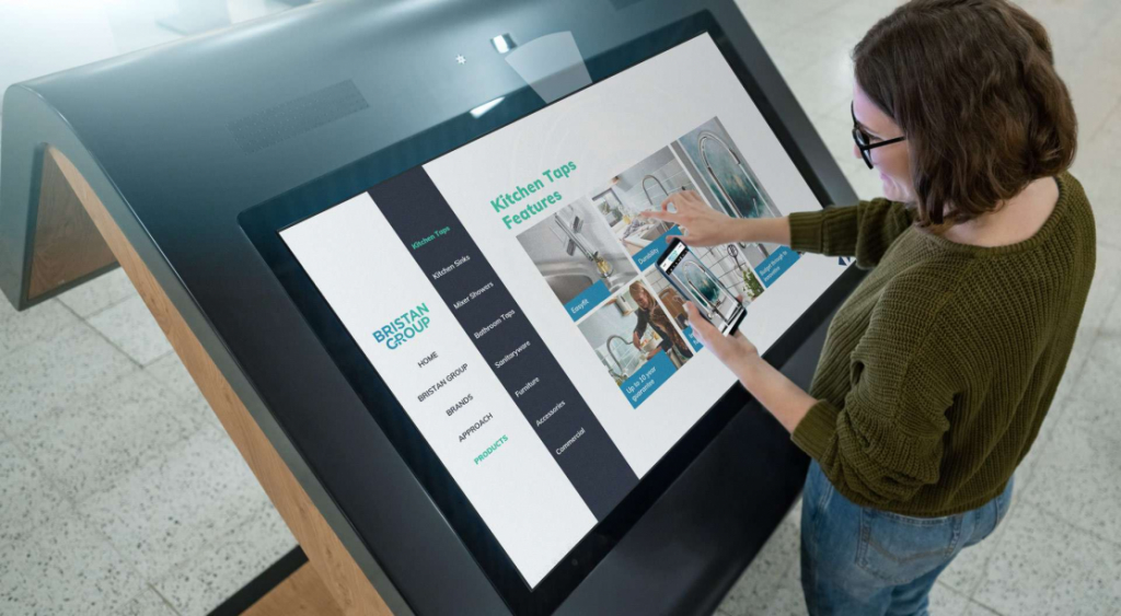 woman using a mobile phone in front of a large interactive touchscreen and she is interacting with products on both devices