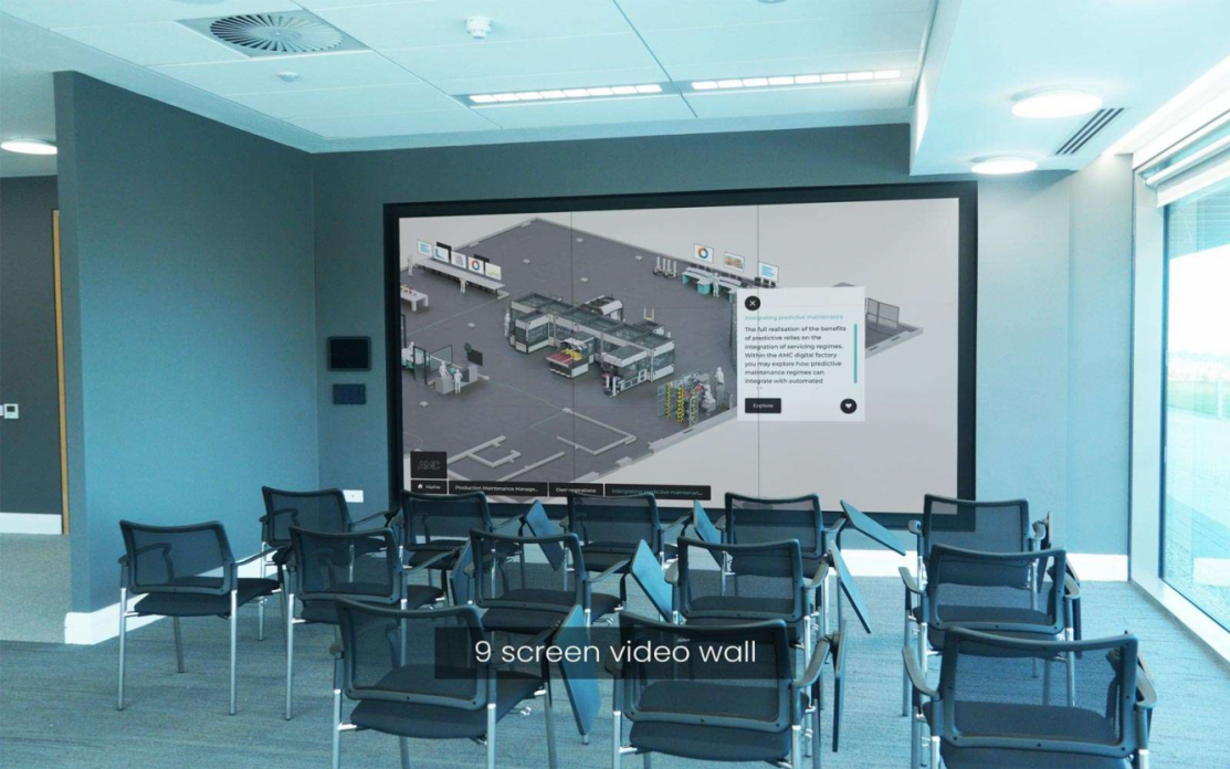 Giant nine-screen interactive video wall in an innovation centre displaying a 3d image of an advanced engineering factory which is controlled from an iPad, there are chairs in front of the screen