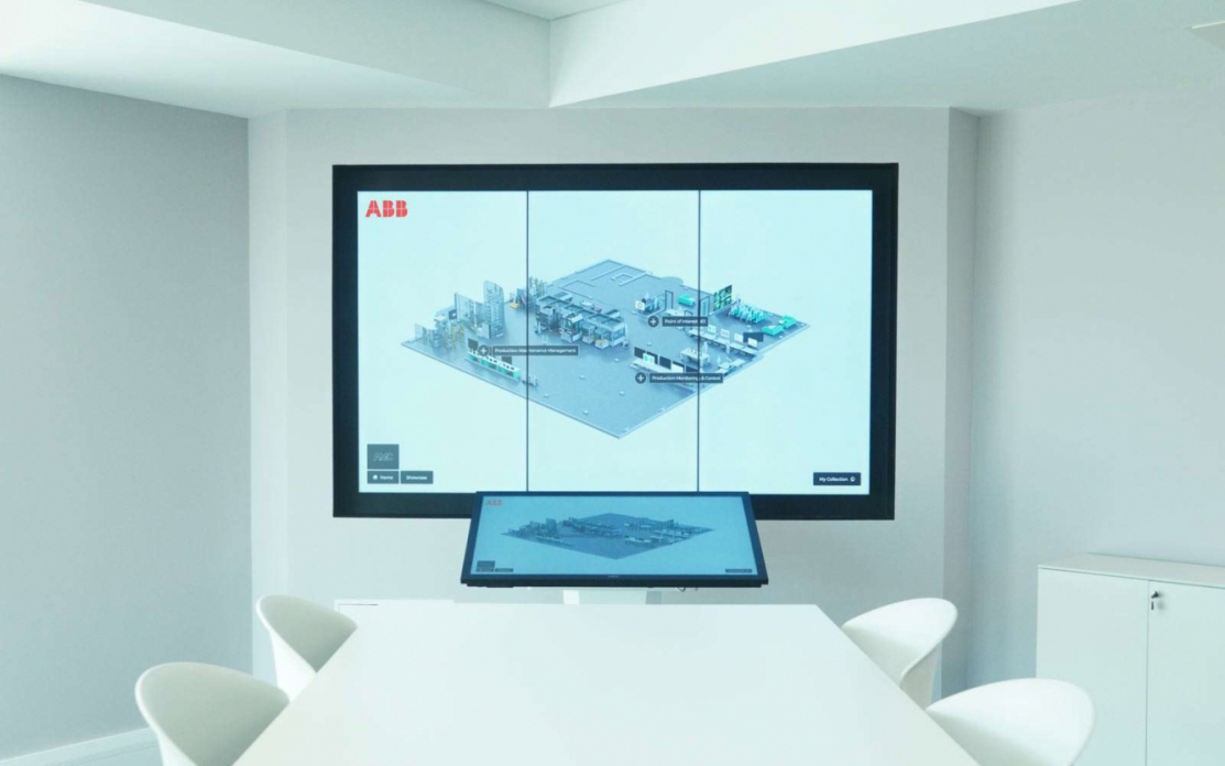 Interactive video wall in a white innovation centre displaying a 3d image of an advanced engineering factory which is controlled from a touchscreen