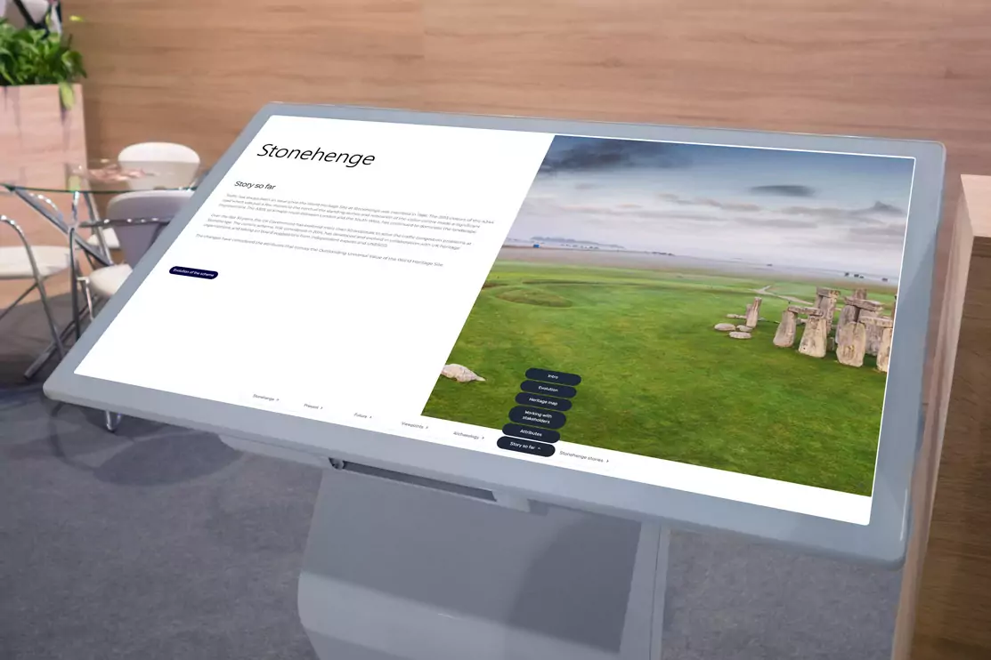 Large white interactive touchscreen in a meeting room with an image of stonehenge, there are chairs and a glass table in the background